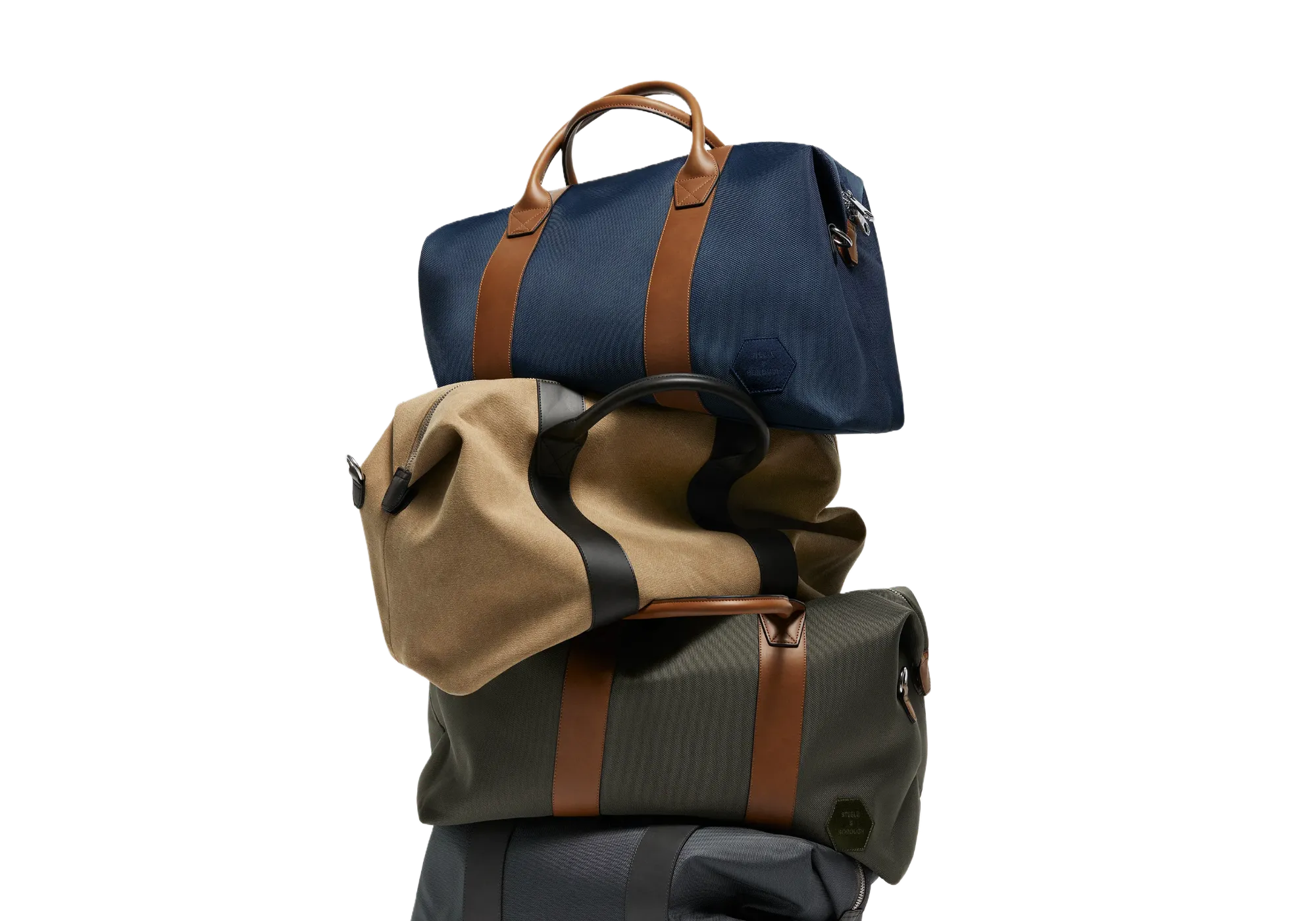 A stack of Steele & Borough weekender bags in an array of colors including navy blue, tan, and olive green, each featuring the signature tan straps and the discreet logo, signifying versatility and style